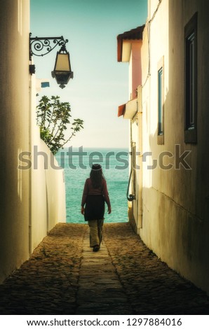 Woman walking away in an alley between houses into the sea