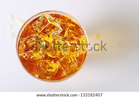 Top view on alcoholic drink in a glass with ice cubes and spilled drops on the table