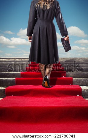 Elegant woman in black coat climbing a red carpet stairway