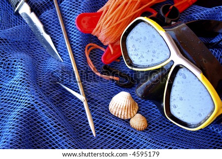 Details of scuba-diving and spear-fishing gear over a blue fishing net bag