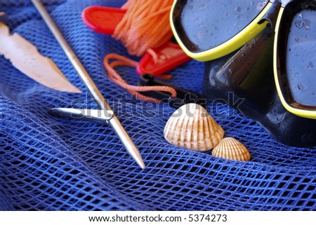 Details of scuba-diving and spear-fishing gear over a blue fishing net bag