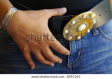 Close-up photo of belt buckle and female hand with bracelet.