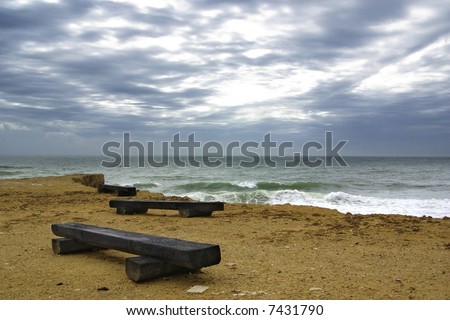 Three wooden benches and stormy sea under deep dark clouds.