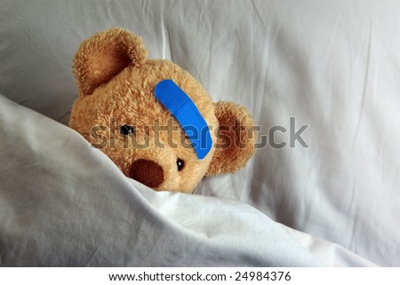 Photo of a sick teddy bear with a blue bandage in bed