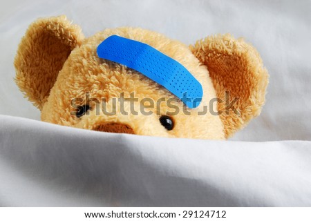 Photo of a sick teddy bear with a blue bandage in bed