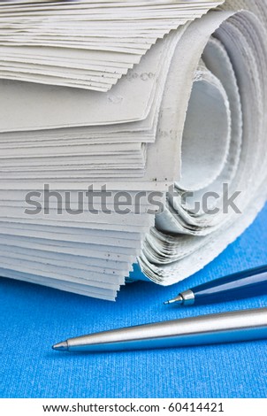 Closeup of a newspaper roll on a blue table with two pens by the side