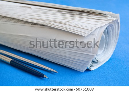 Closeup of a newspaper roll on a blue table with two pens by the side