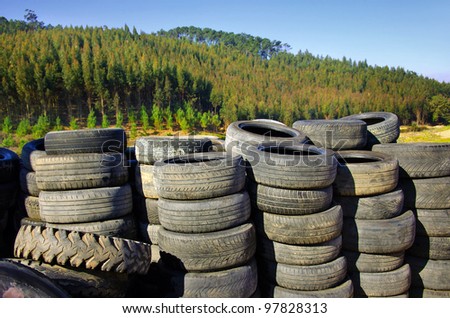 Piles of old and worn out automobile tires for recycling near a field of trees