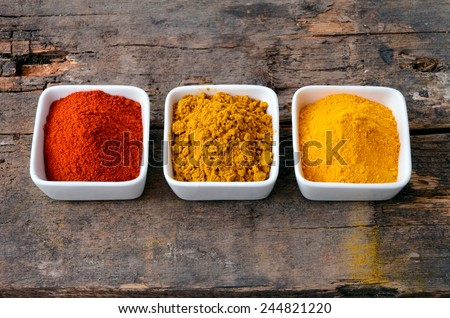 Hot red chili powder, curry and turmeric powder on wooden background