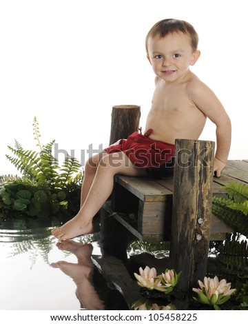 An adorable preschool swimmer ready to slide into the water from a rustic old dock.  The dock is surrounded by water foliage.  On a white background.
