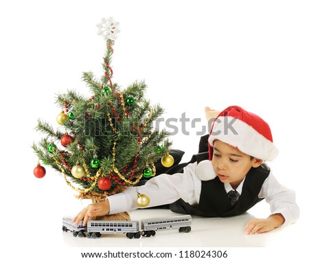 A kindergarten boy driving his toy train around a tiny Christmas tree.  On a white background.