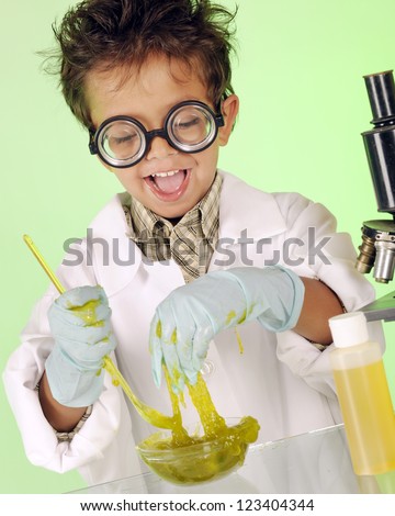 An adorable preschooler with wild hair and coke-bottle glasses delightedly  handling a bowl of yucky, green slime.
