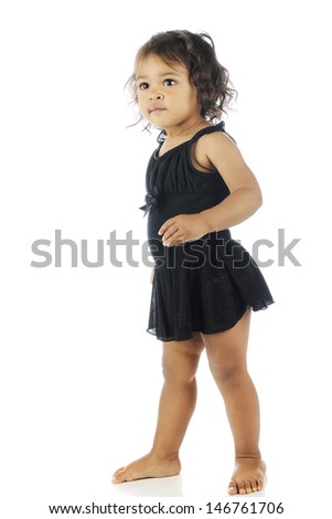 An adorable toddler barefoot in her black ballerina dress.  On a white background.