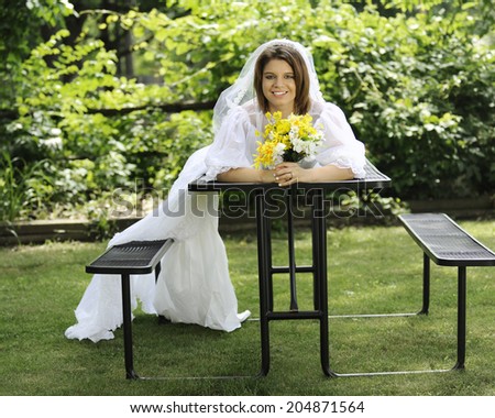 A beautiful young bride laying across a picnic table, the train of her gown drooping across a seat to the ground.