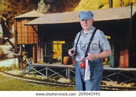 A senior train engineer holding an oil can and rag by an old freight station.