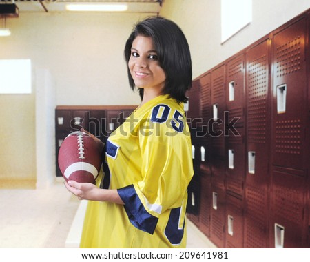 A pretty teen girl happily holding a football in an empty locker room.