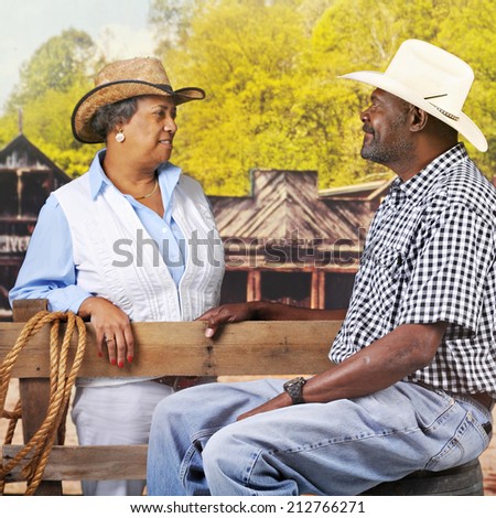 A mature, senior African American couple flirting over a fence in an old western town.