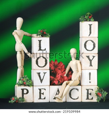 The words Love, Joy and Peace spelled out in rustic alphabet blocks.  Two mannequins, poinsettias and springs of holly adorn them.  All on a background of green and black diagonal stripes.