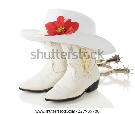 A pair of white cowgirl boots topped by a white hat with a red poinsettia with spurs laying nearby.  On a white background.