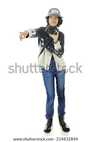 An attractive young teen school photographer with camera in hand, pointing off to her right.  On a white background.