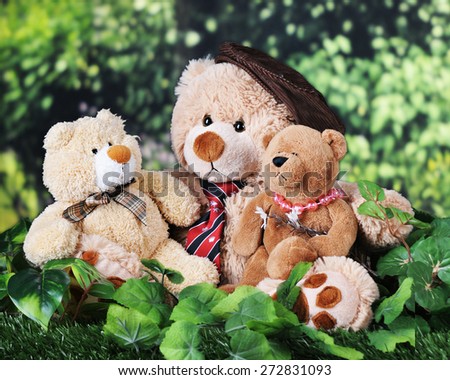 A toy father, son and daughter bear cuddled together on the grass near the woods.