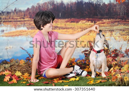 A attractive young teen rewarding her dog with a treat as they play on a warm fall day by the edge of a pond.