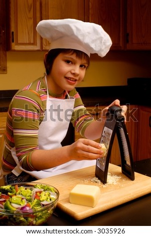 Attractive girl in chef\'s hat and apron grating cheese with a bowl of sliced veggies nearby.