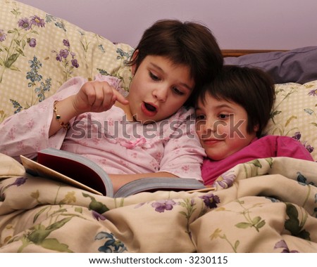 A mid-elementary girl reading a good story to her younger sister in bed.