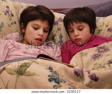 A mid-elementary girl reading a story in bed, her younger sister asleep at her side.