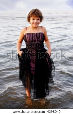 Attractive elementary girl in an evening gown holding up her skirt while cooling her feet in a lake.