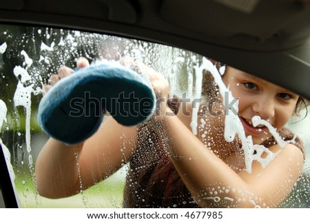 Elementary girl washing a car window viewed from inside the car.