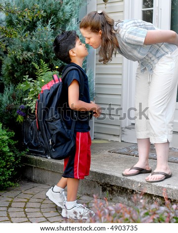 Mother on her front steps kissing her young elementary son good-bye as he heads out to school.