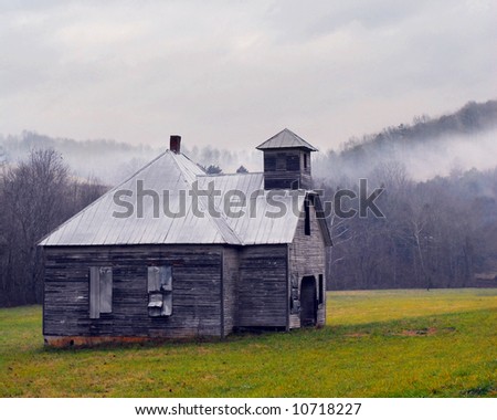 An old one-room school house in the Smokey Mountains, a fog rising in the distance above late autumn trees.