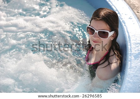 A preteen girl soaking in an outdoor hot tub on a sunny day.