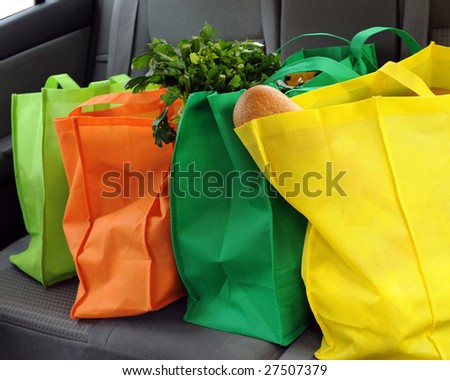 Four colorful eco-friendly shopping bags filled mostly with groceries in the back seat of a car.