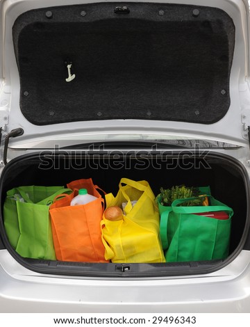 Four colorful eco-friendly shopping bags filled mostly with groceries in the opened trunk of a car.  Open trunk provides negative space for your message.