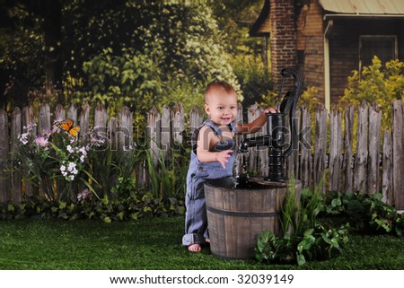 An adorable one-year-old happily playing with an old water pump by an old farm house.