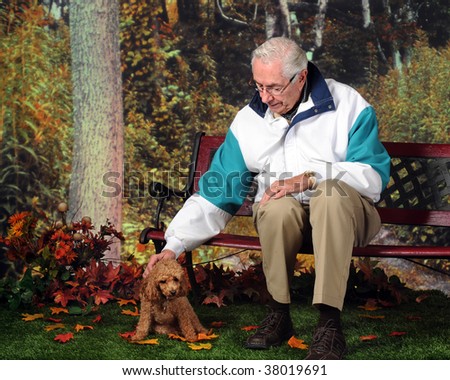 A senior man on a park bench in the fall petting his pet poodle.