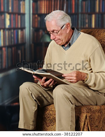A senior man studying a book in an office or home library.