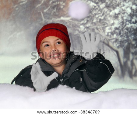 A happy kindergarten boy catching a snowball from behind a snow bank.  Motion blur on snowball.