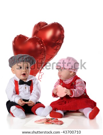 A baby girl and boy, dressed for a big date, snacking on heart-shaped cookies together.  Isolated on white.