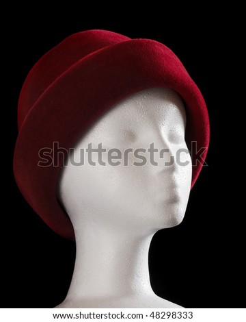 A white styrofoam model of a woman\'s head wearing a soft, red hat.  Dramatic lighting.  Isolated on black.