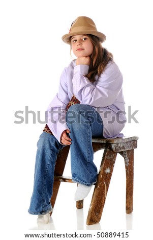 A serious preteen girl dressed in her grandpa\'s shirt, tie and hat while sitting on an old step stool.  Isolated on white.