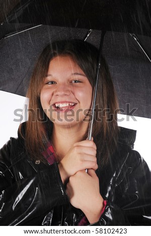 A young teen happily in her raincoat and under a black umbrella  in the rain.