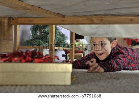 A young elementary boy in his pajamas reaching toward a wrapped gift under his parents\' bed.