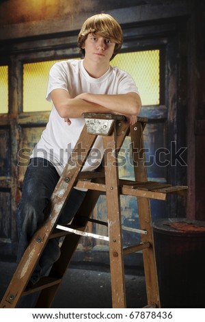 A serious young teen boy on a ladder in an old garage.