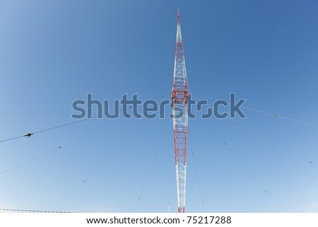 A red and white weather station antenna with guide wires and lightning arresters.  All against a clear, deep blue sky.