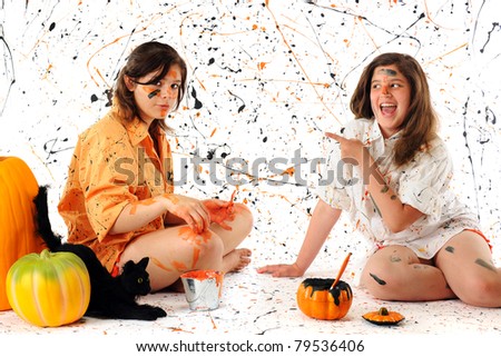 A teen and preteen making a Halloween mess with black and orange pain.  A black cat and pumpkins nearby.