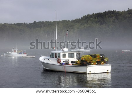 A lobster boat loaded with trips in a harbor with other boats where a morning mist remains.