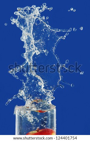 splash and spray water into the vessel from a fallen apple, photo on the blue background.